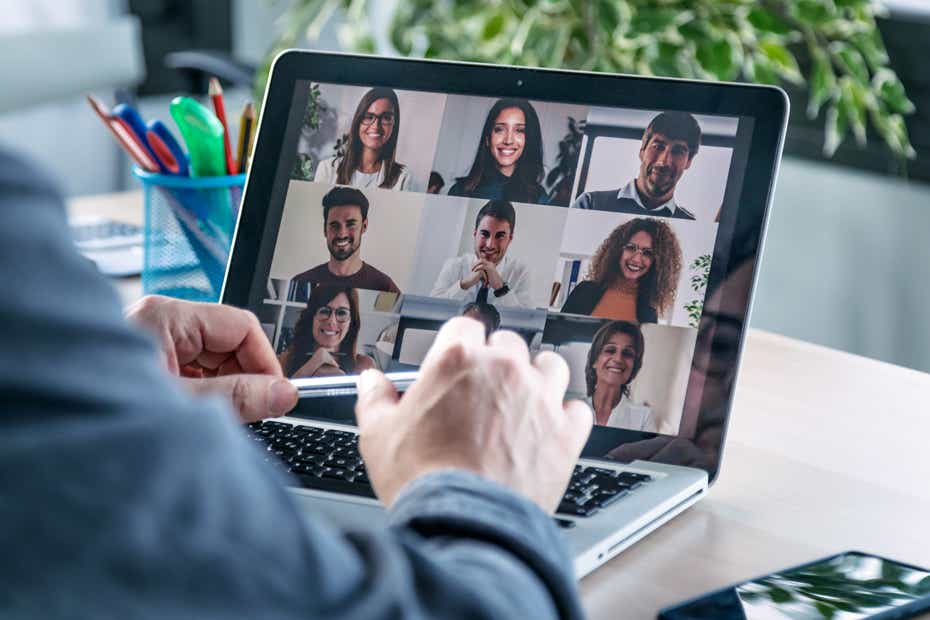 A person sits in front of a laptop screen that shows a group of colleagues meeting online